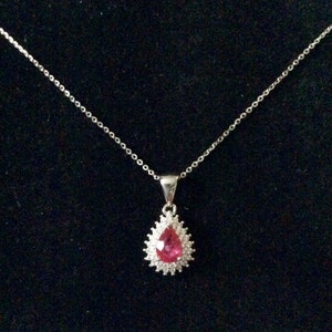 Peut inclure: Un collier en chaîne argent avec un pendentif en forme de larme. Le pendentif présente une pierre précieuse rose entourée de petites pierres précieuses claires.