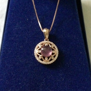 Peut inclure: Un collier en or rose avec un pendentif orné d'une pierre précieuse ronde de couleur mauve clair entourée d'un délicat sertissage de diamants.