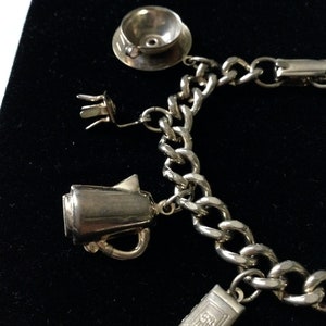 Pode incluir: Um bracelete de prata com uma variedade de pingentes, incluindo uma ch&aacute;vena de ch&aacute;, um bule e um livro. O bracelete &eacute; feito de uma corrente grossa e robusta.