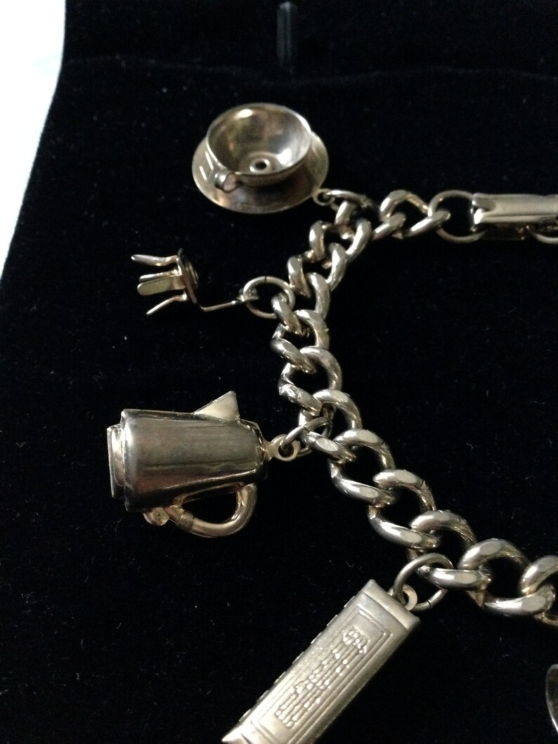 Pode incluir: Um bracelete de prata com uma variedade de pingentes, incluindo uma ch&aacute;vena de ch&aacute;, um bule e um livro. O bracelete &eacute; feito de uma corrente grossa e robusta.