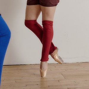 May include: Three people wearing leg warmers. The person on the left is wearing blue leg warmers and a black skirt. The person in the middle is wearing red leg warmers and a brown skirt. The person on the right is wearing gray leg warmers and a light blue skirt.