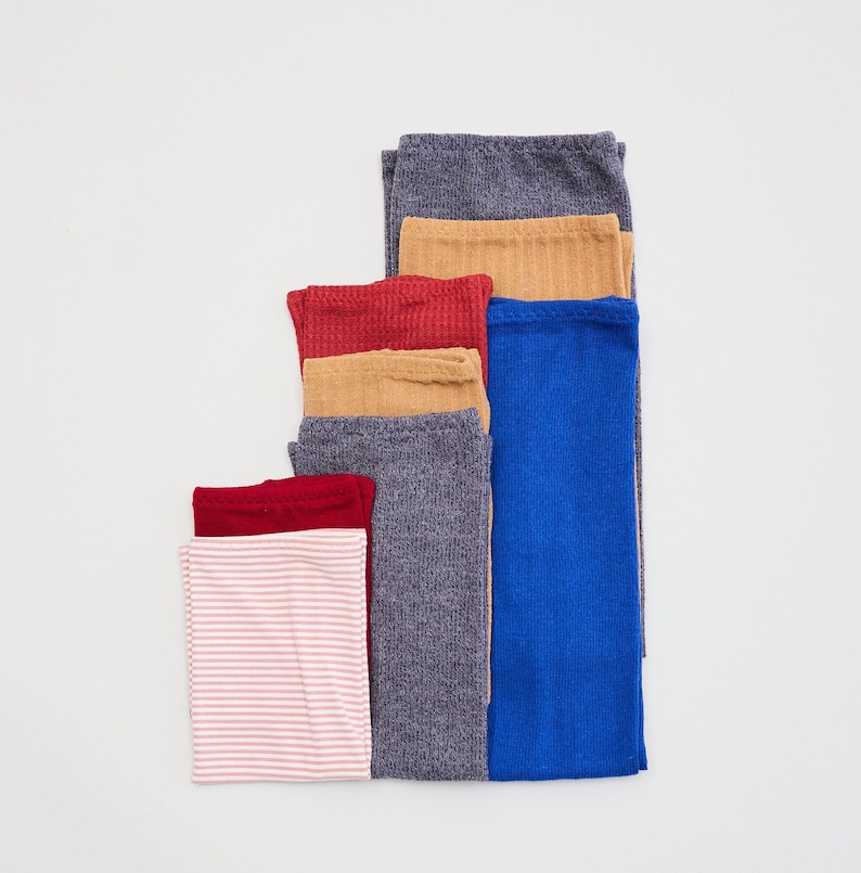 May include: A stack of seven ribbed leggings in various colors, including pink, red, brown, gray, and blue.