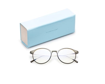 May include: A pair of round, grey-framed glasses with blue light blocking lenses. The glasses are resting on a white surface next to a light blue glasses case with the word "HARBOUR2" printed on it.