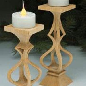 May include: Two wooden candle holders with a natural finish. Each holder has a square base, a decorative central support, and a square top holding a battery-operated candle with a flickering flame. The candle holders are approximately 8 inches tall.