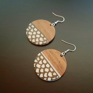 May include: A pair of round wooden earrings with a white and brown geometric pattern. The earrings have silver hooks.