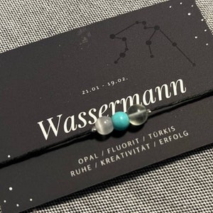 May include: Black card with white text that reads "Wassermann 21.01 - 19.02."  The card also has a constellation symbol and the text "Opal / Fluorit / Türkis Ruhe / Kreativität / Erfolg".