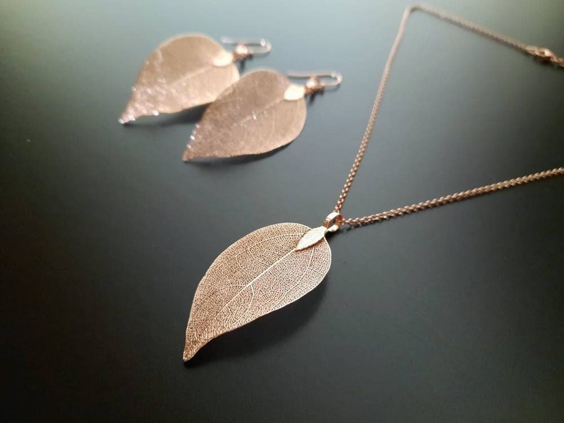 May include: A delicate rose gold necklace and earrings set featuring leaf-shaped pendants. The leaves are made of thin, intricate metalwork and have a delicate, airy appearance.