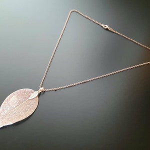 May include: A rose gold necklace with a delicate leaf pendant. The leaf is detailed with a textured surface and a smaller leaf detail.