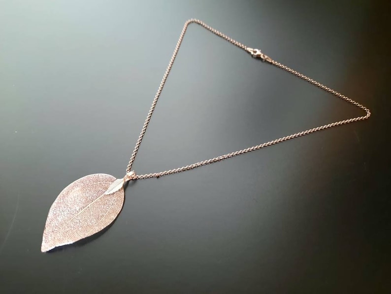 May include: A rose gold necklace with a delicate leaf pendant. The leaf is detailed with a textured surface and a smaller leaf detail.
