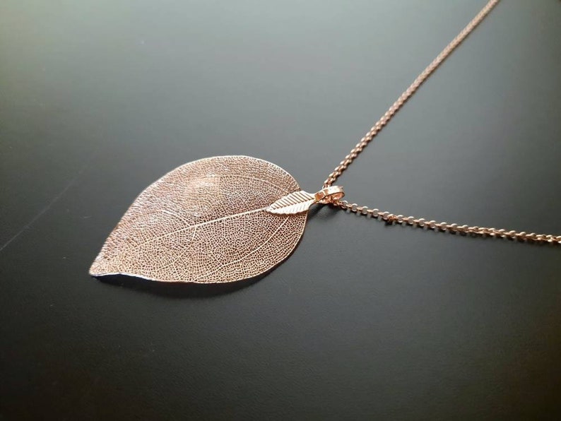 May include: A delicate rose gold necklace with a leaf pendant. The leaf is made of a thin metal and has a detailed vein pattern.