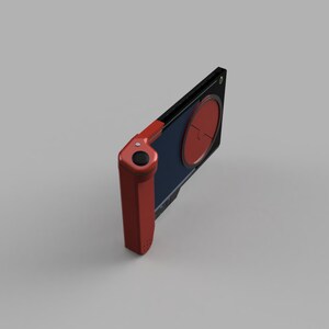 Op de afbeelding: Een rood en zwart draagbaar spelapparaat met een ronde knop aan de zijkant en een scherm met een rode cirkel.