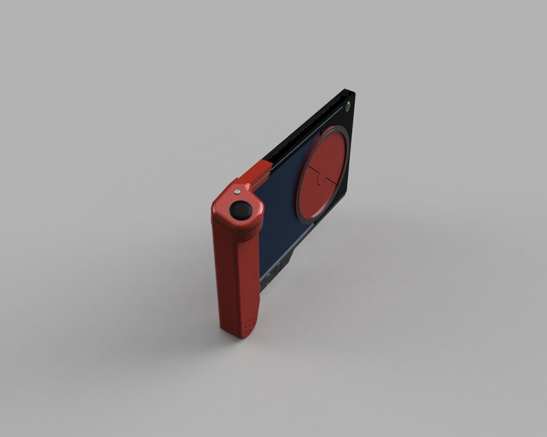 Op de afbeelding: Een rood en zwart draagbaar spelapparaat met een ronde knop aan de zijkant en een scherm met een rode cirkel.