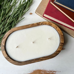 May include: A white candle with three wicks in a wooden bowl. The bowl is oval shaped and has a dark brown stain.