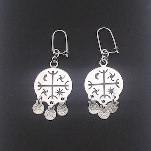 May include: A pair of silver earrings with a circular design featuring a cross, moon, stars, and other symbols. The earrings have four small, round charms hanging from the bottom.