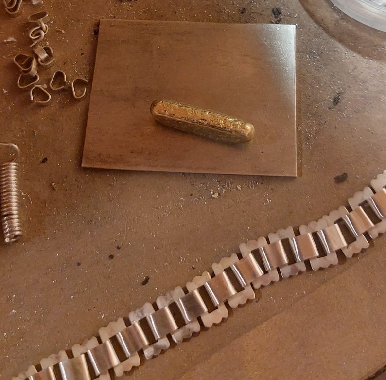 May include: A gold-colored metal bar on a gray surface, next to a gold-colored metal chain with square links.