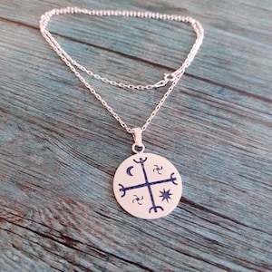 May include: Silver necklace with a round pendant featuring a silver cross with a crescent moon, star, and other symbols.