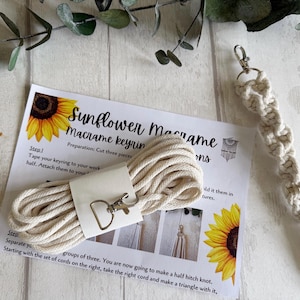 May include: A macrame keychain kit with instructions. The kit includes a bundle of cream-coloured cord, a silver-tone clasp, and a finished macrame keychain. The instructions feature a sunflower graphic and the text "Sunflower Macrame keynin".