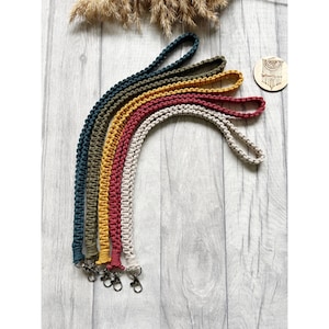 May include: Five colourful crocheted lanyards with metal clasps. The lanyards are in shades of green, yellow, red, beige, and dark green.