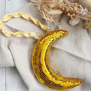 May include: A gold crescent moon-shaped disco ball with a yellow and white braided rope handle.