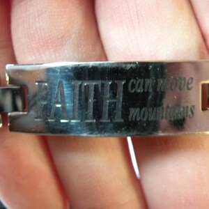 May include: A silver bracelet with a metal band that reads "FAITH can move mountains".