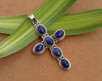 May include: A silver cross pendant with seven oval-shaped lapis lazuli stones. The stones are a deep blue color and are set in silver.