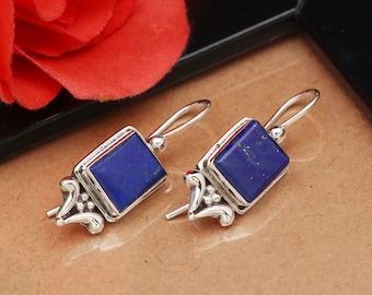 May include: A pair of silver earrings with blue lapis lazuli stones. The stones are set in a square shape and the earrings have a delicate, ornate design.