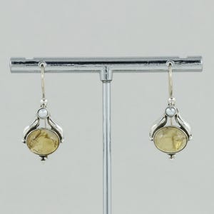 May include: A pair of silver dangle earrings featuring a yellow gemstone and a white pearl accent.