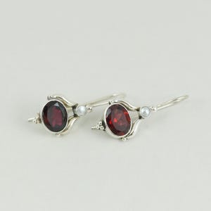 May include: A pair of silver dangle earrings with red gemstone and white pearl accents.