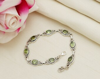 May include: A silver bracelet with a chain link design and oval-shaped green gemstones.