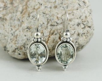Puede incluir: Un par de pendientes colgantes de plata con piedras preciosas ovaladas de color verde pálido. Los pendientes tienen un diseño decorativo con una pequeña bola en la parte superior e inferior, y un gancho para la oreja. Las piedras están engastadas en un marco de plata.