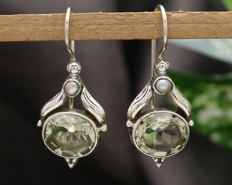 Puede incluir: Un par de pendientes colgantes de plata con una piedra preciosa verde y detalles de perlas.