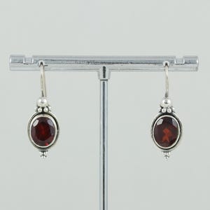 May include: A pair of silver dangle earrings with red gemstone accents. The earrings feature a round, faceted gemstone set in a silver bezel.