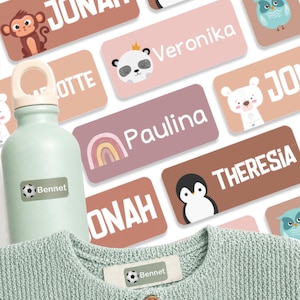 May include: A light green water bottle and a light green knit garment, both featuring rectangular adhesive labels with the name Bennet and a soccer ball graphic. Several other rectangular labels with various names and animal illustrations are scattered.