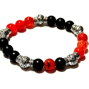 May include: A beaded bracelet featuring alternating black and red-orange gemstone beads. The bracelet has decorative silver-colored metal spacers. The beads are round and smooth, creating a striking contrast in color and texture.