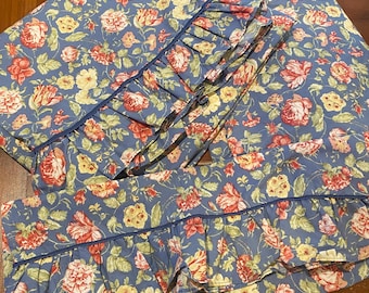 Puede incluir: Un juego de fundas de almohada de tela azul con un estampado floral de rosas rojas, rosas y amarillas y hojas verdes. Las fundas están decoradas con un volante fruncido en los bordes, rematado con un fino ribete de color azul oscuro.