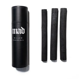 May include: Black cylindrical container with the word "mad" in white, and the words "WILLOW CHARCOAL" below it. Three black charcoal sticks are next to the container. The items are on a white background.