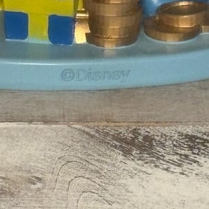 May include: A light blue Disney figurine base with gold coins, a stack of gold coins, and a blue and yellow block. The word "Disney" is printed on the base.
