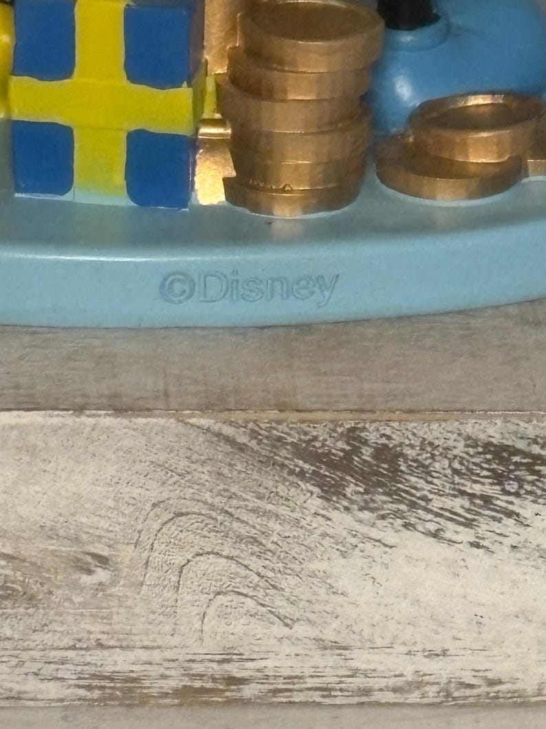 May include: A light blue Disney figurine base with gold coins, a stack of gold coins, and a blue and yellow block. The word "Disney" is printed on the base.
