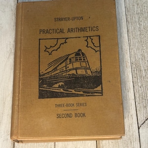 May include: A vintage textbook titled "PRACTICAL ARITHMETICS" by Strayer-Upton. The cover is tan with black text and a black illustration of a train. The book is part of the "THREE-BOOK SERIES" and is the "SECOND BOOK".