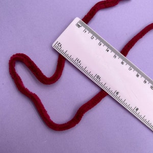 May include: A close-up of a burgundy velvet cord measuring 10 inches long against a purple background.