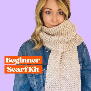 May include: A beginner scarf kit with a light beige scarf worn by a person with long blonde hair. The scarf is made of a soft, chunky yarn and has a simple, textured stitch pattern. The text "Beginner Scarf Kit" is displayed in orange letters on a red background.