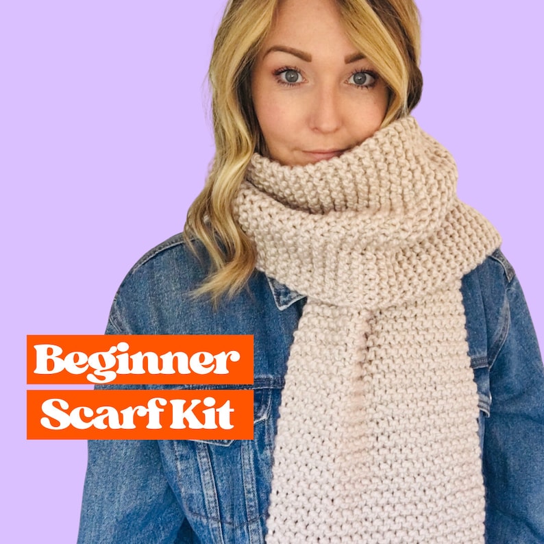 May include: A beginner scarf kit with a light beige scarf worn by a person with long blonde hair. The scarf is made of a soft, chunky yarn and has a simple, textured stitch pattern. The text "Beginner Scarf Kit" is displayed in orange letters on a red background.