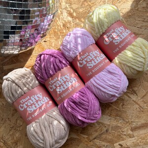 May include: Four skeins of yarn in different colors: beige, pink, light purple, and yellow. Each skein has a label that says "That Crafty Stitch The Squishy One".