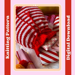 Puede incluir: Una bolsa de regalo de punto de rayas rojas y blancas con un lazo rojo. La bolsa está llena de regalos envueltos y está sobre una superficie blanca y peluda. La imagen es de una descarga digital para un patrón de tejido de punto.