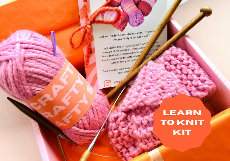 May include: A pink learn to knit kit with two bamboo knitting needles, a ball of pink yarn, and a partially knitted pink scarf. The kit comes in a box with the words "Learn to Knit Kit" on a bright orange circle.
