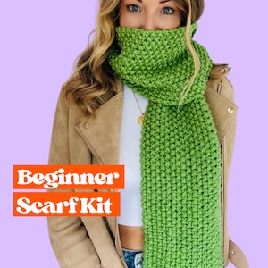 May include: A beginner scarf kit featuring a green knitted scarf. The scarf is shown being worn by a person with long brown hair. The text "Beginner Scarf Kit" is displayed in orange letters on a white background.