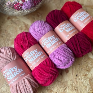 May include: Five spools of yarn in various shades of pink and red. Each spool has a label that reads "That Crafty Stitch The Squishy One".