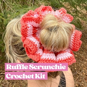 Könnte beinhalten: Ein rosa und korallenfarbenes Häkel-Scrunchie mit Rüschen-Design. Das Scrunchie wird im Haar einer Frau getragen. Der Text "Ruffle Scrunchie Crochet Kit" ist unter dem Scrunchie zu sehen.