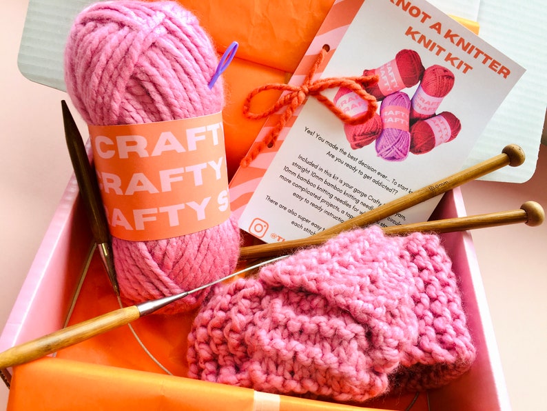 May include: A pink knitting kit containing a ball of yarn, two wooden knitting needles, and a partially knitted pink scarf. The kit includes instructions and is labelled "Not a Knitter Knit Kit".