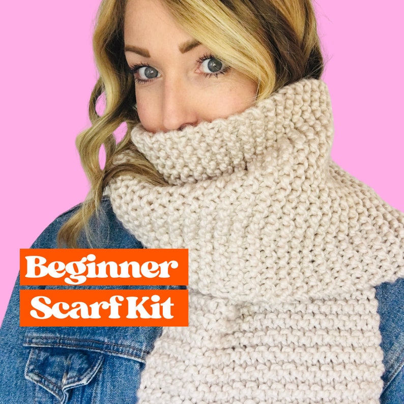 May include: A woman wearing a beige knitted scarf. The scarf is thick and textured. The text "Beginner Scarf Kit" is displayed in orange letters on a white background.